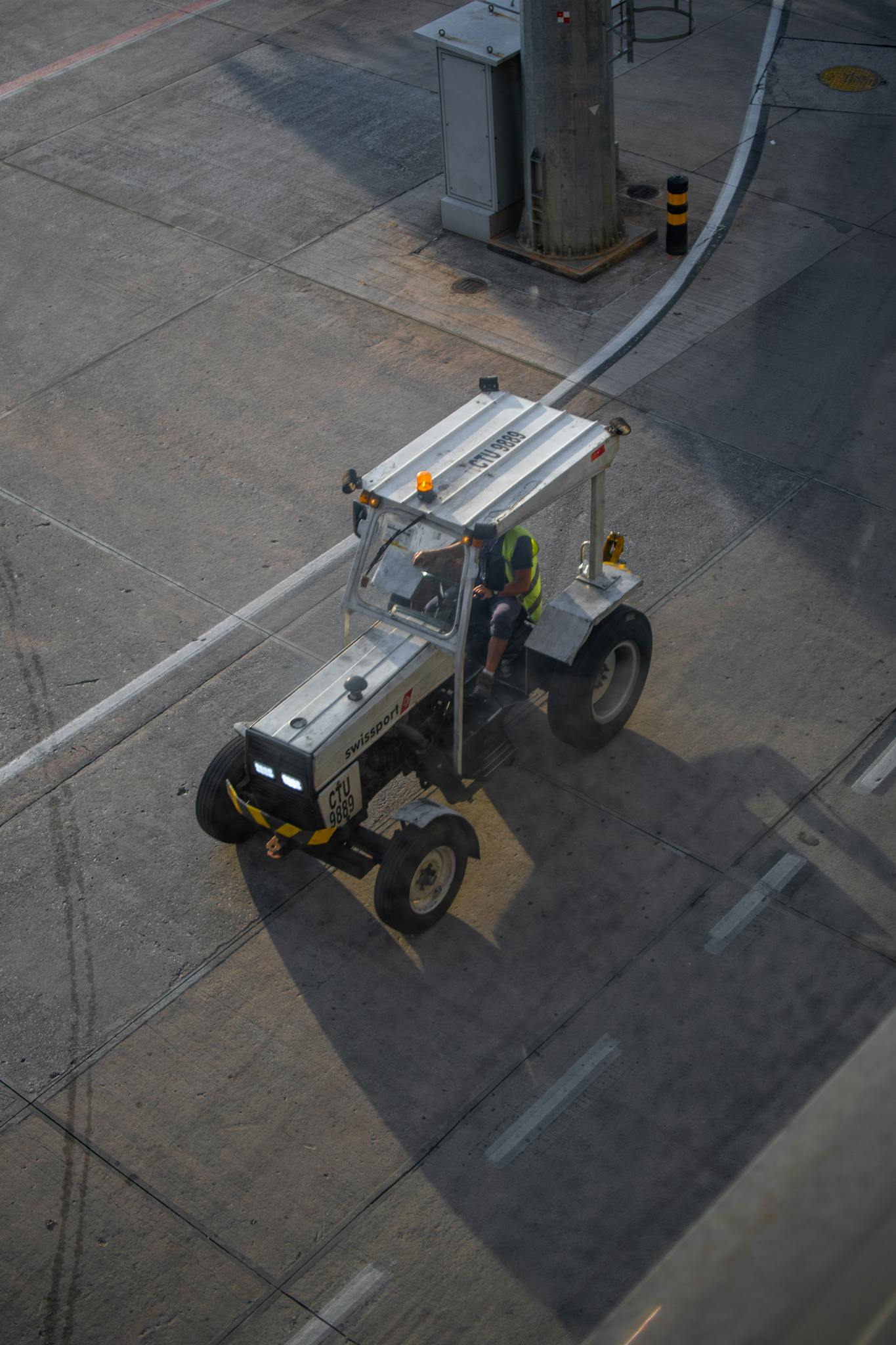 A worker operates an industrial vehicle on the airport tarmac during sunset.